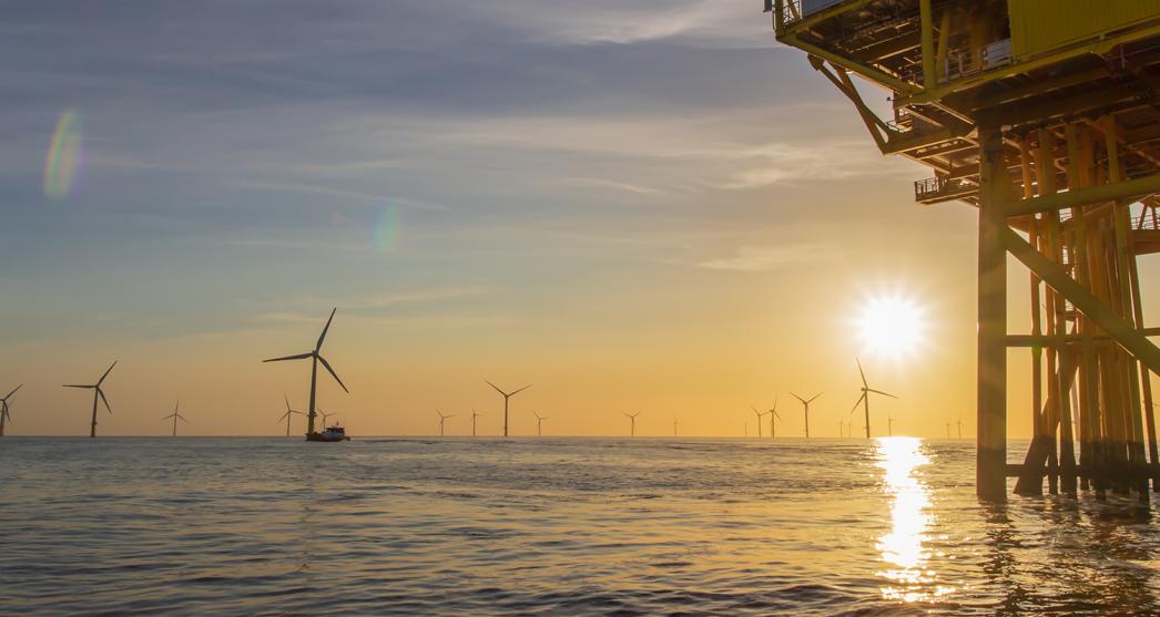A photo of an offshore wind farm with a part of a coverter station visible on the right