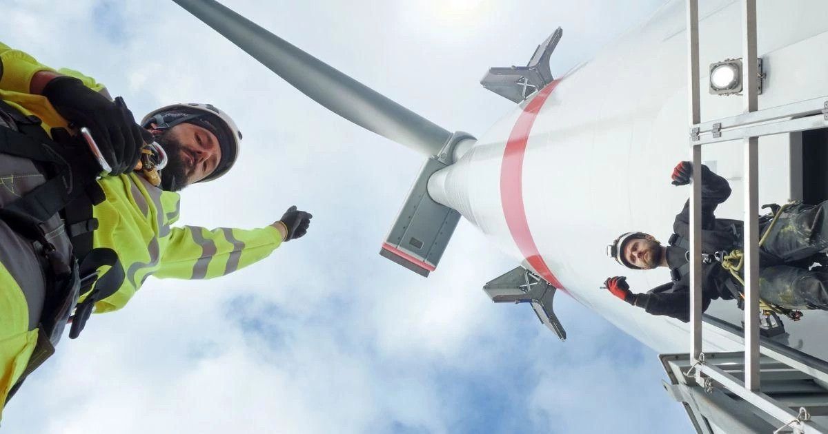 A photo of a wind turbine technician next to a wind turbine