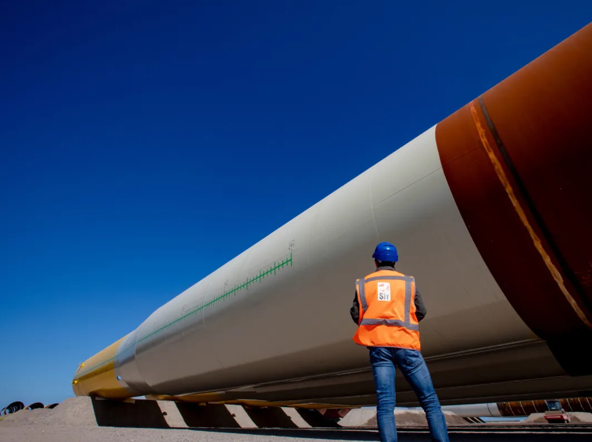 A photo showing an extra large monopile lying at Sif's production site with Sif worker in front