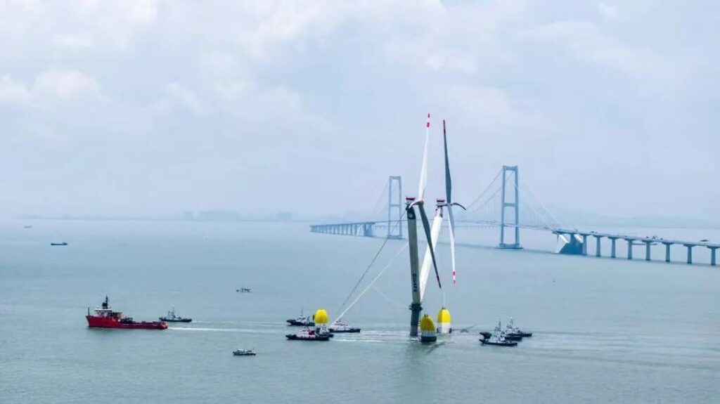 OceanX floating wind turbine being towed near a bridge