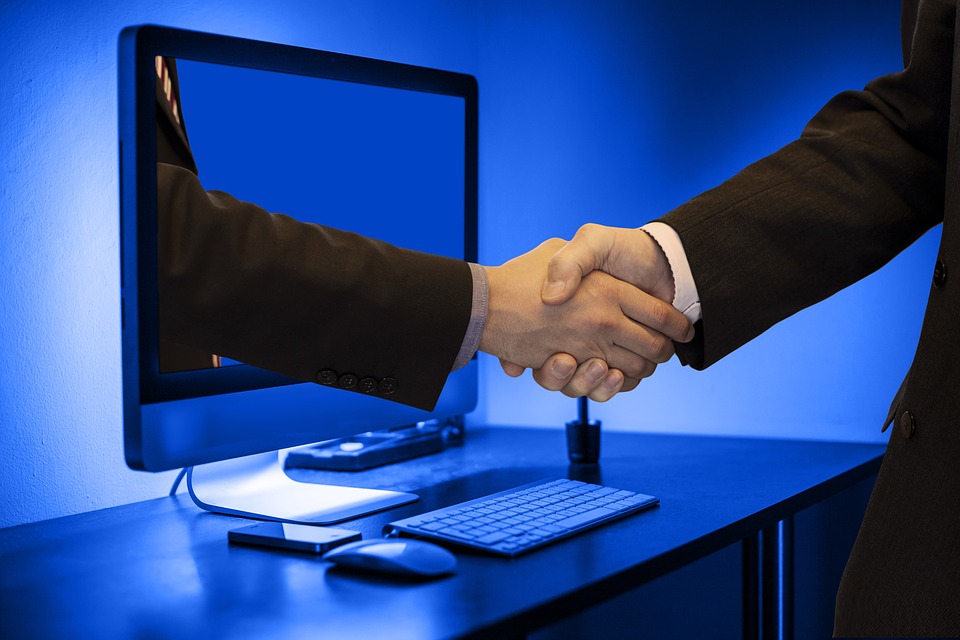 An illustrative image showing handshake through a computer monitor