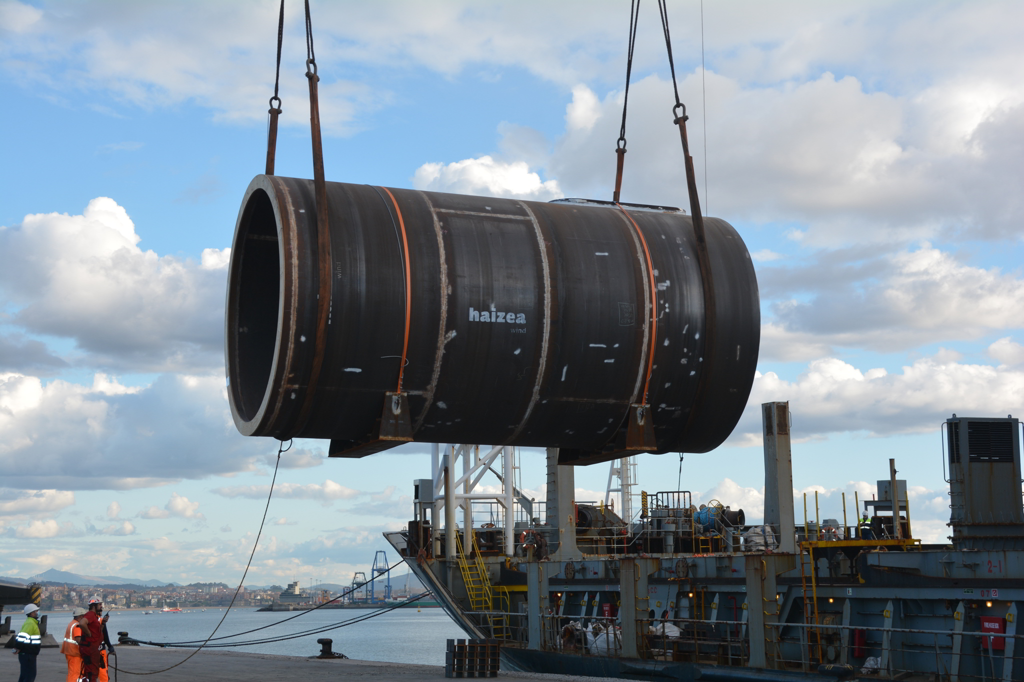 A transition piece barrel being loaded by a crane onto a transport vessel in Bilbao