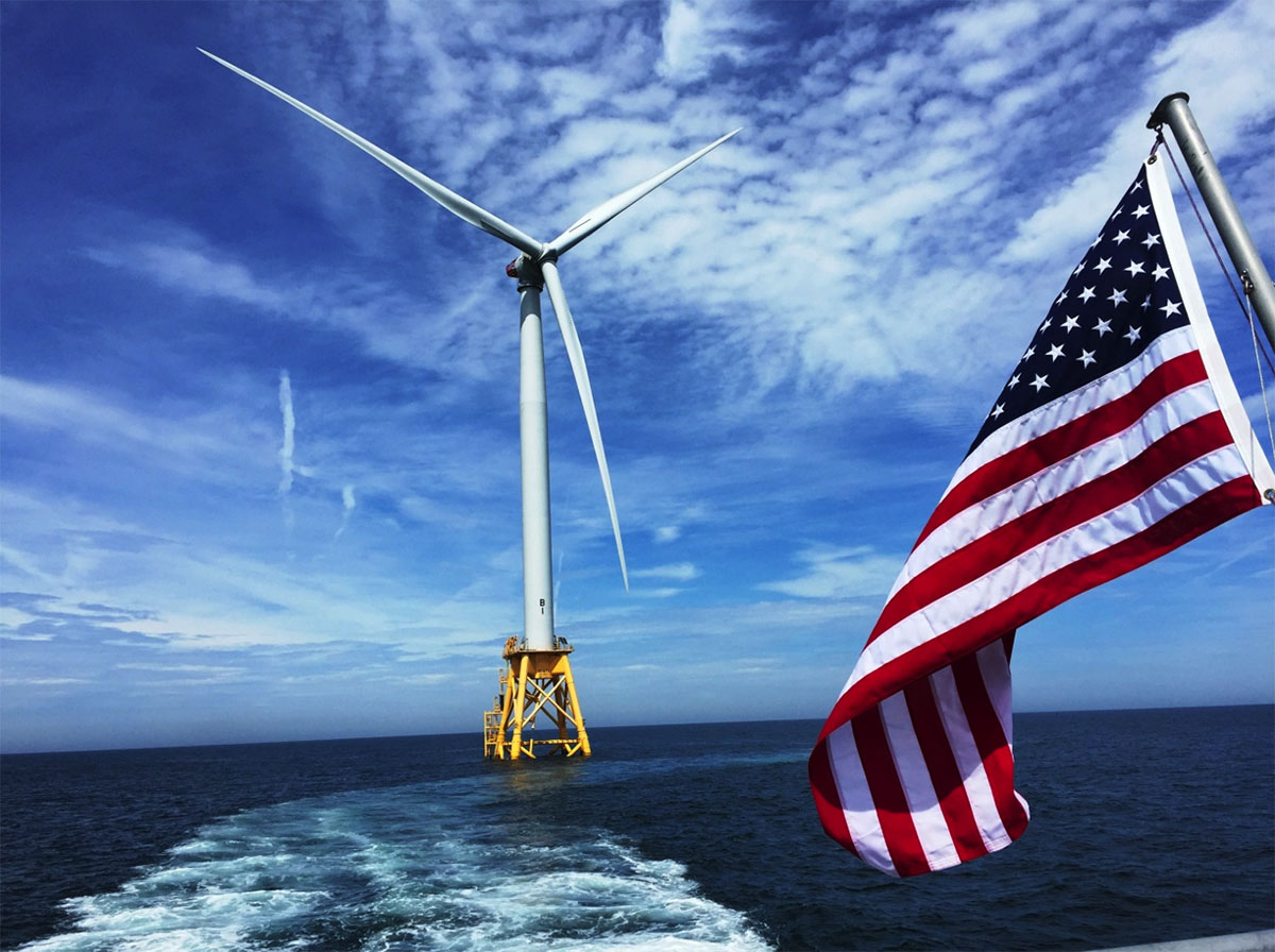 A wind turbine at the Block Island Offshore Wind Farm with a U.S. flag on a vessel visible in the right corner