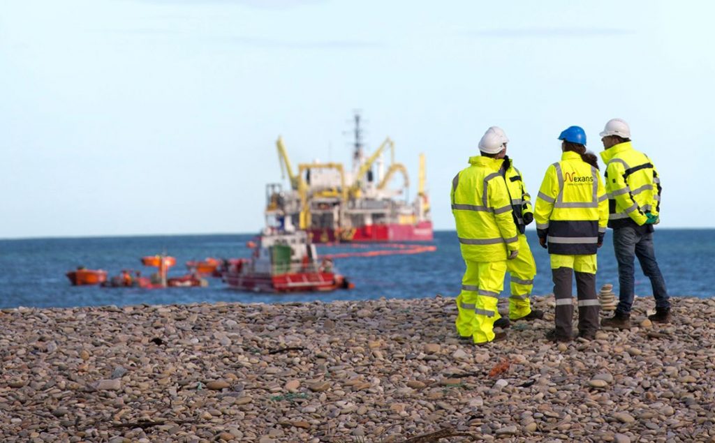 Nexans crew on a beach with Nexans cable laying vessel at sea