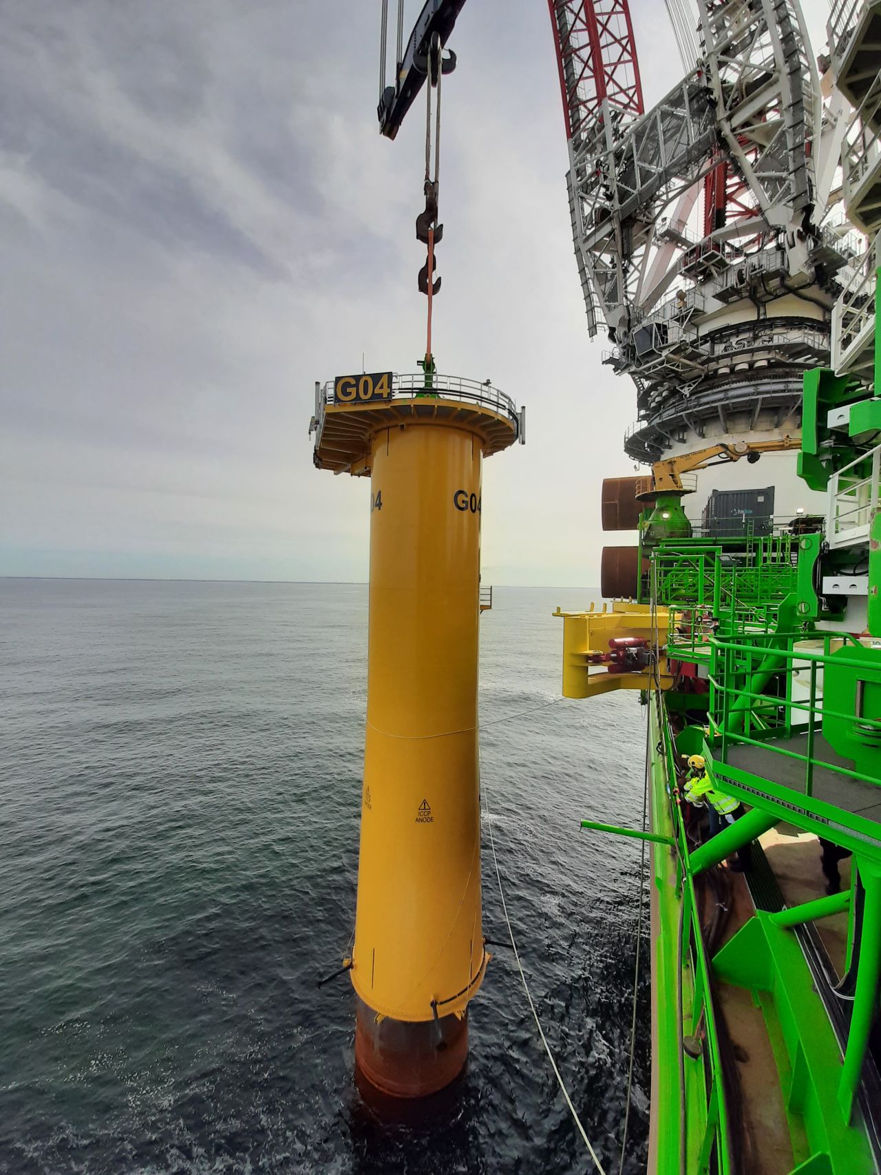 A photo taken from DEME's Innovation vessel during the installation of a yellow transition piece on top of a monopile at Saint-Nazaire offshore site