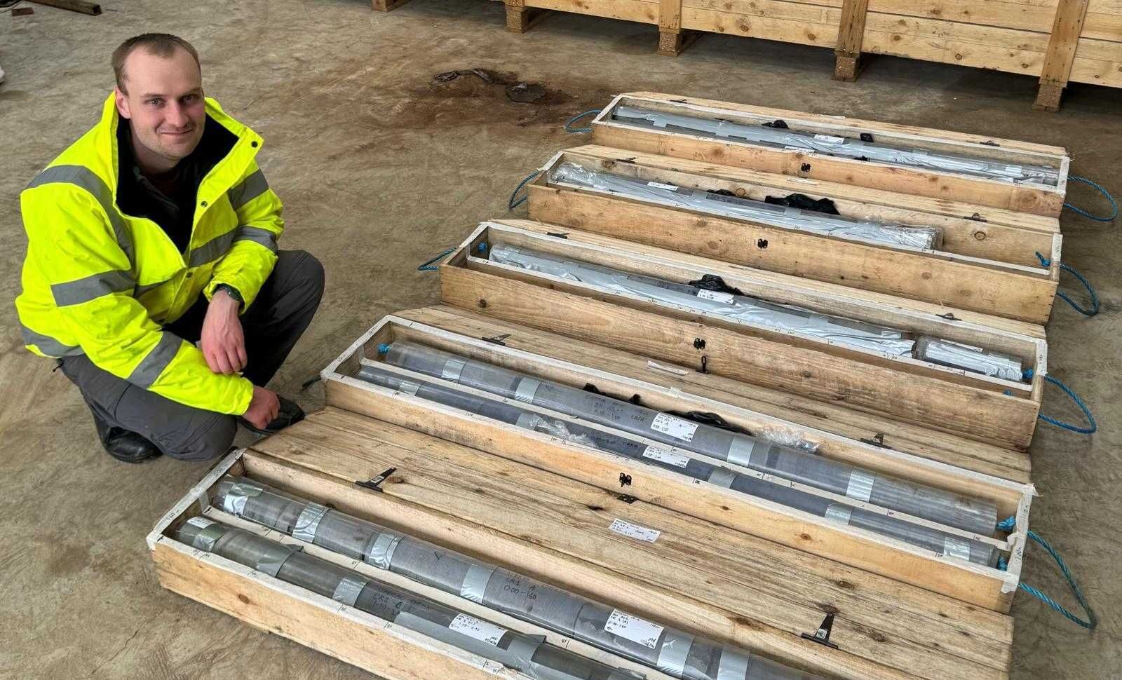 A man in his working suit, Matthew Hewitson, squats next to the tidal turbine parts