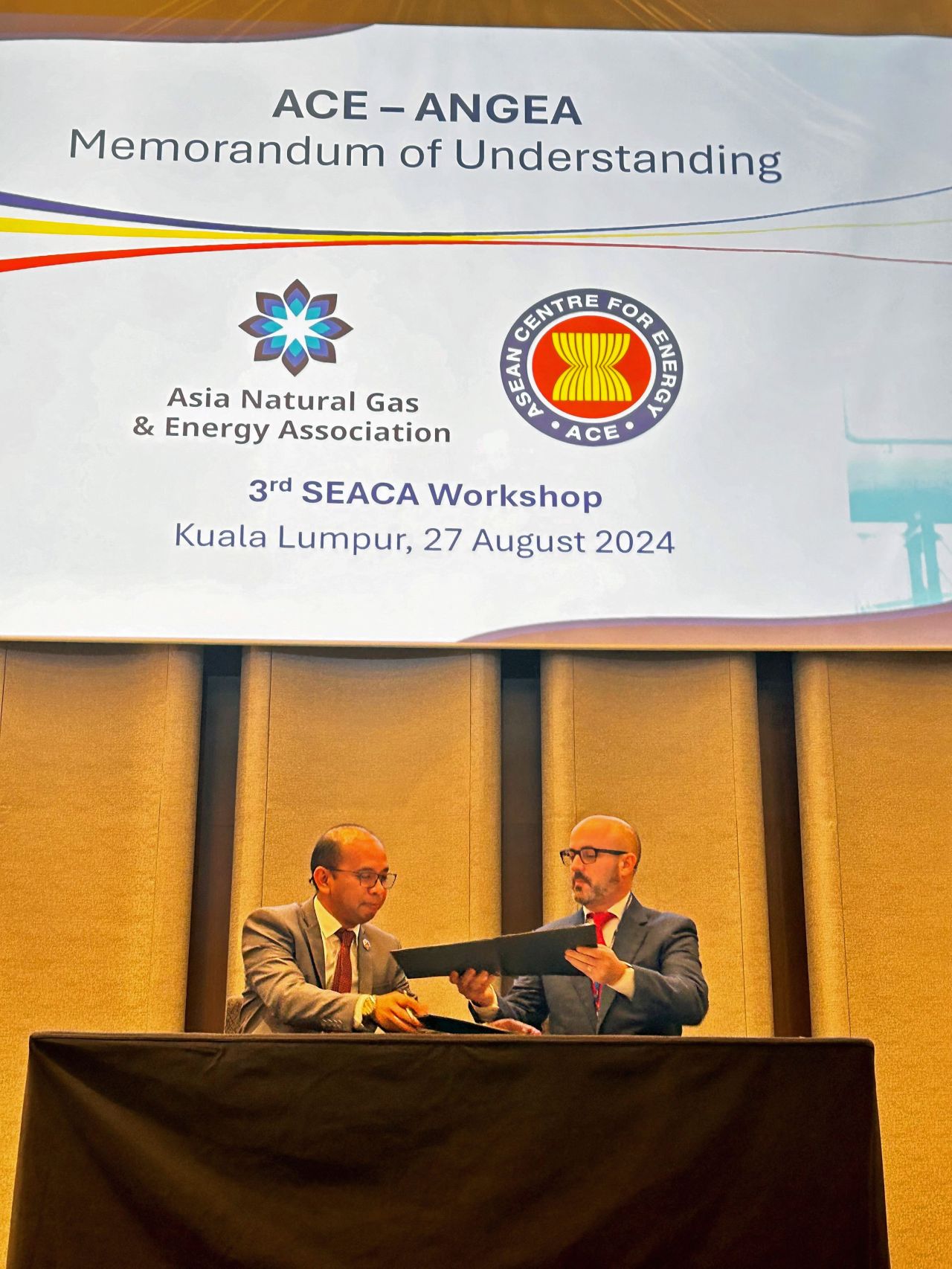 Two men sitting behind a desk exchanging documents