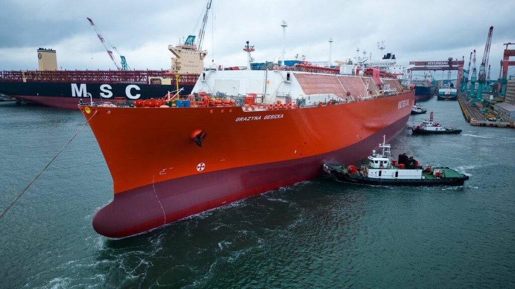 A vessel leaving the shipyard surrounded by several tugboats