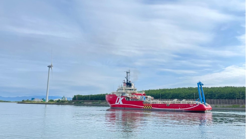 A photo of the vessel MV Kaiyu sailing next to a wind turbine in a port