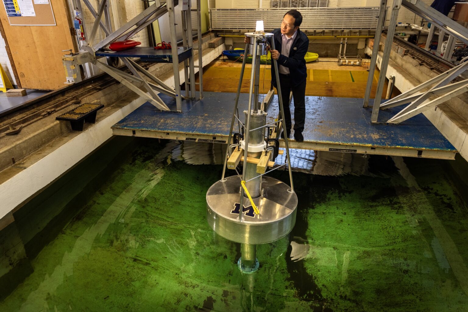 Inside the University of Michigan’s Marine Hydrodynamics Laboratory, Lei Zuo, the Herbert C. Sadler Collegiate Professor of Engineering and a professor of naval architecture and marine engineering, inspects a prototype buoy that generates electricity from wave motion. Whenever the buoy bobs up or down, the light blinks on. Image credit: Marcin Szczepanski, Michigan Engineering.