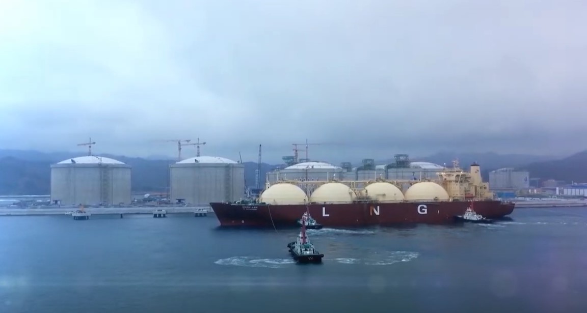 A large vessel with LNG written on the side near the shore with four plants