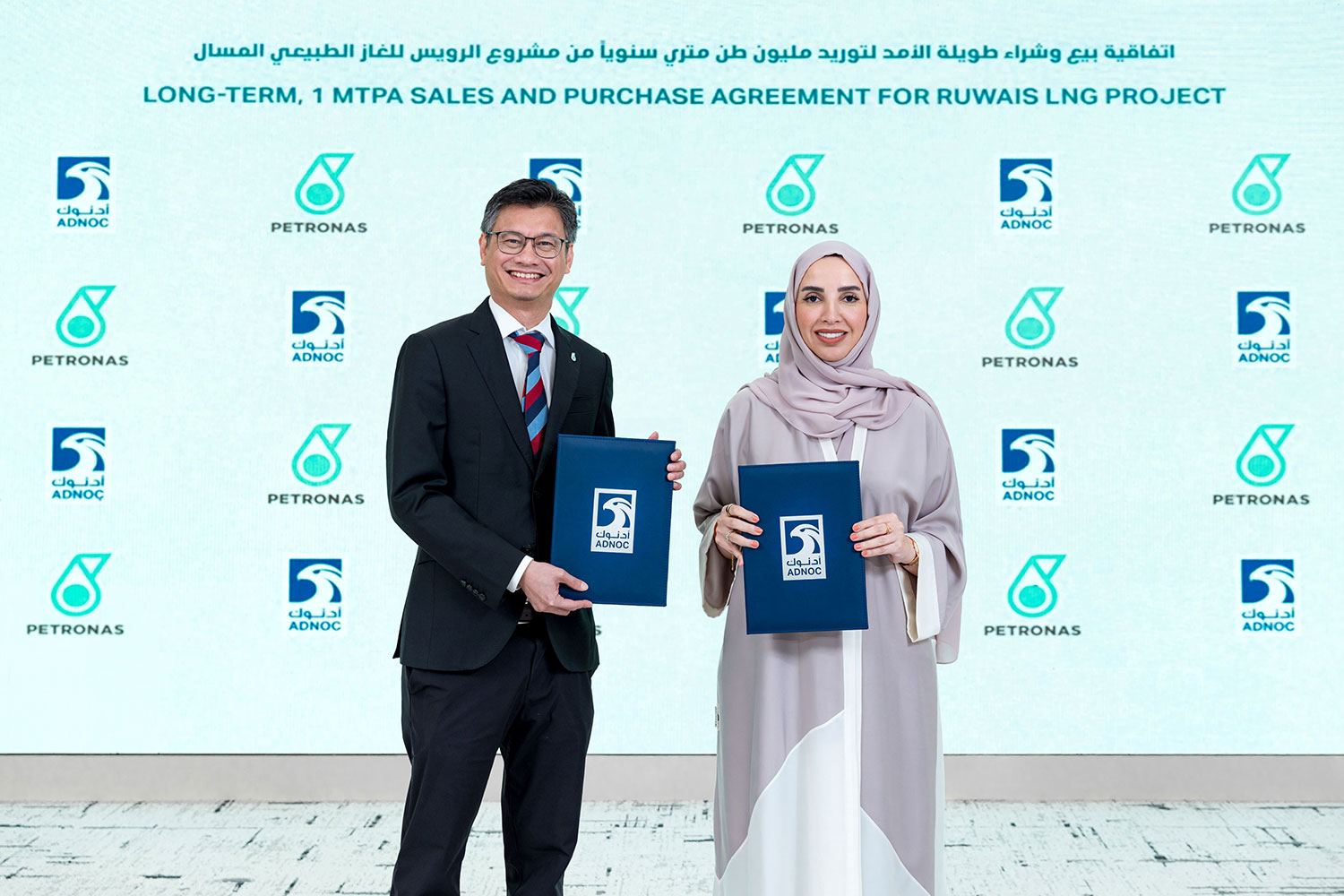 A woman and a man standing and holding files with ADNOC's logo on them